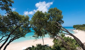 A beach with clear turquoise waters, white sand, and lush green trees. - Coral Cove 11 by Altman (Paynes Bay)