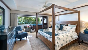A four-poster bed with a nautical theme, a dark wooden dresser, a blue armchair, and a view of the outdoors through large windows. - Coral Cove 11 by Altman (Paynes Bay)