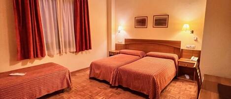 Una habitación de hotel con suelo de parquet de madera, una cama con colcha a rayas rojas, una banca, un escritorio y una lámpara colgante.