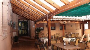 An outdoor dining area with wooden tables and chairs, a covered patio, and a brick wall with a 'HOTEL' sign. - Hotel Las Tablas (Daimiel)