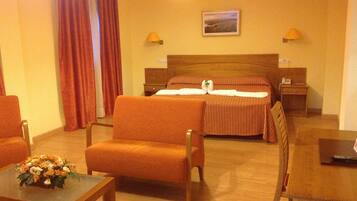Een hotelkamer met een bed, twee nachtkastjes, een bureau, een stoel en een kleintje tafeltje met bloemen.