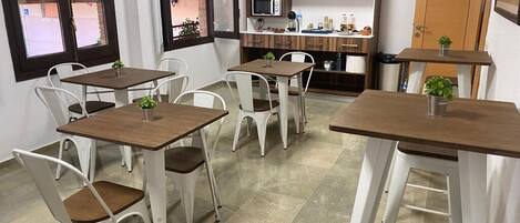 A compact kitchen with wooden cabinets, a microwave, and a small dining area with white chairs and tables.