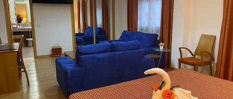 A hotel room with a large bed, a blue sofa, a desk, and a TV.