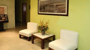 A lobby with two white chairs, a small table with a vase of flowers, and a framed landscape painting on the wall. - Hotel Las Tablas (Daimiel)