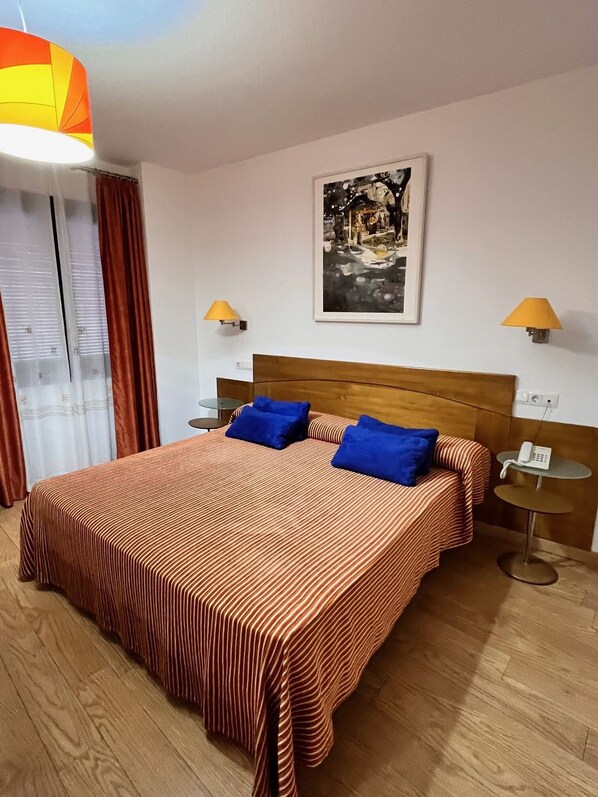 Una habitación de hotel con una cama grande, dos mesitas de noche, un teléfono y un cuadro en la pared.