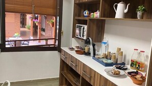 A compact kitchen with wooden cabinets, a microwave, and various kitchen items. - Hotel Las Tablas (Daimiel)