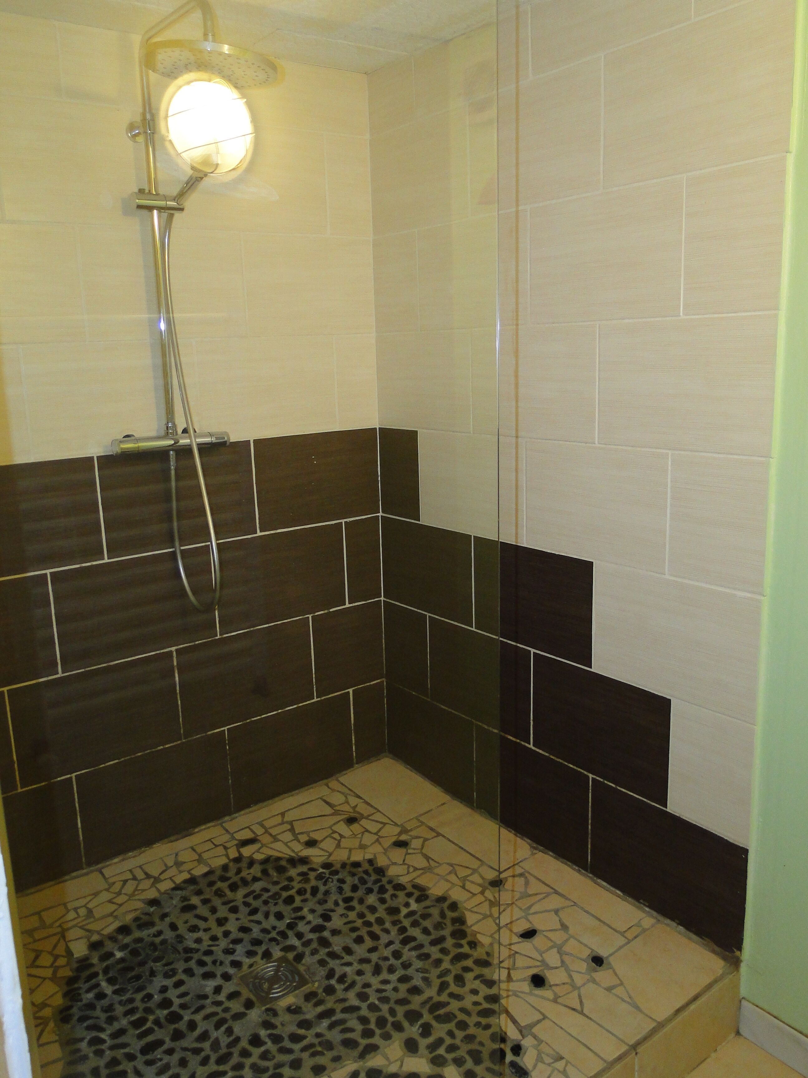 A shower area with a glass door, tiled walls, and a patterned floor.