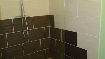 A shower area with a glass door, tiled walls, and a patterned floor.