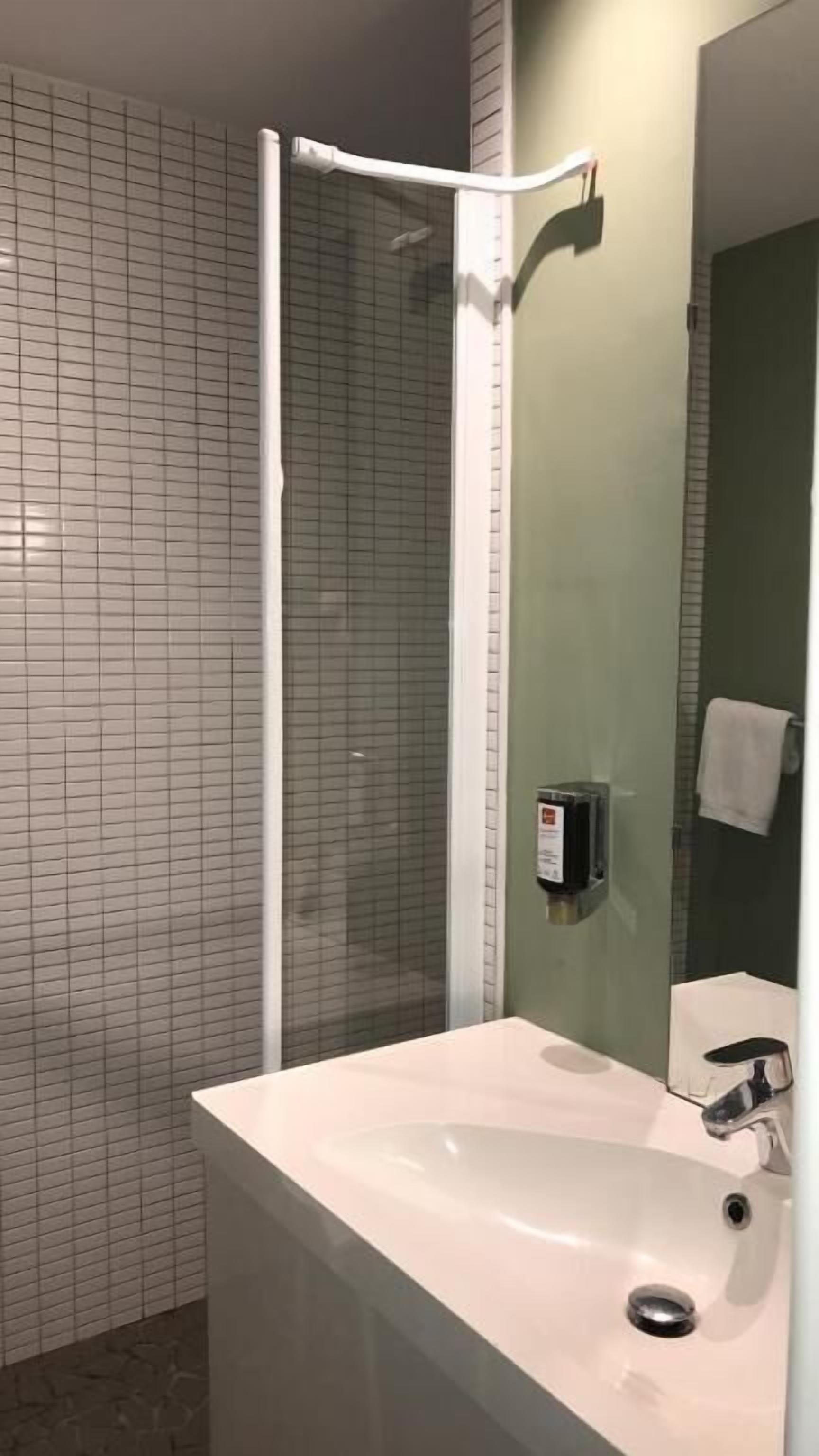 Un bagno con un lavandino bianco, box doccia in vetro e specchio.