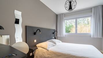 A modern hotel room with a bed, a desk, and a chair.