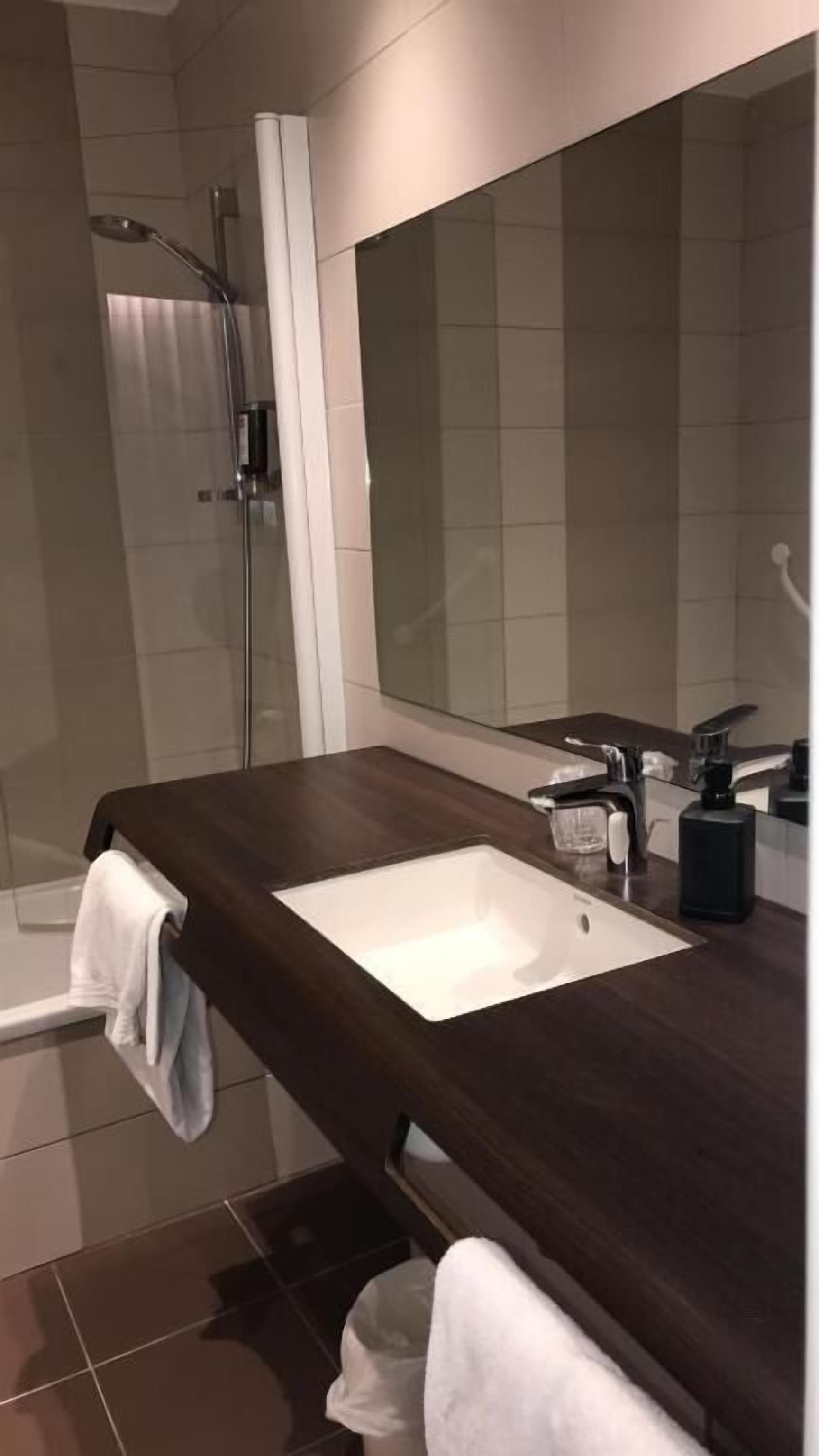 Un baño moderno con tocador de madera oscura, un lavamanos blanco y un espejo grande.