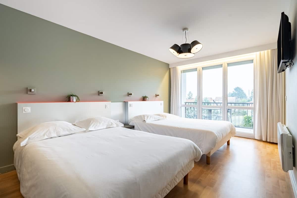 A modern hotel room with two beds, a large window with a view, a ceiling light, and a TV mounted on the wall.