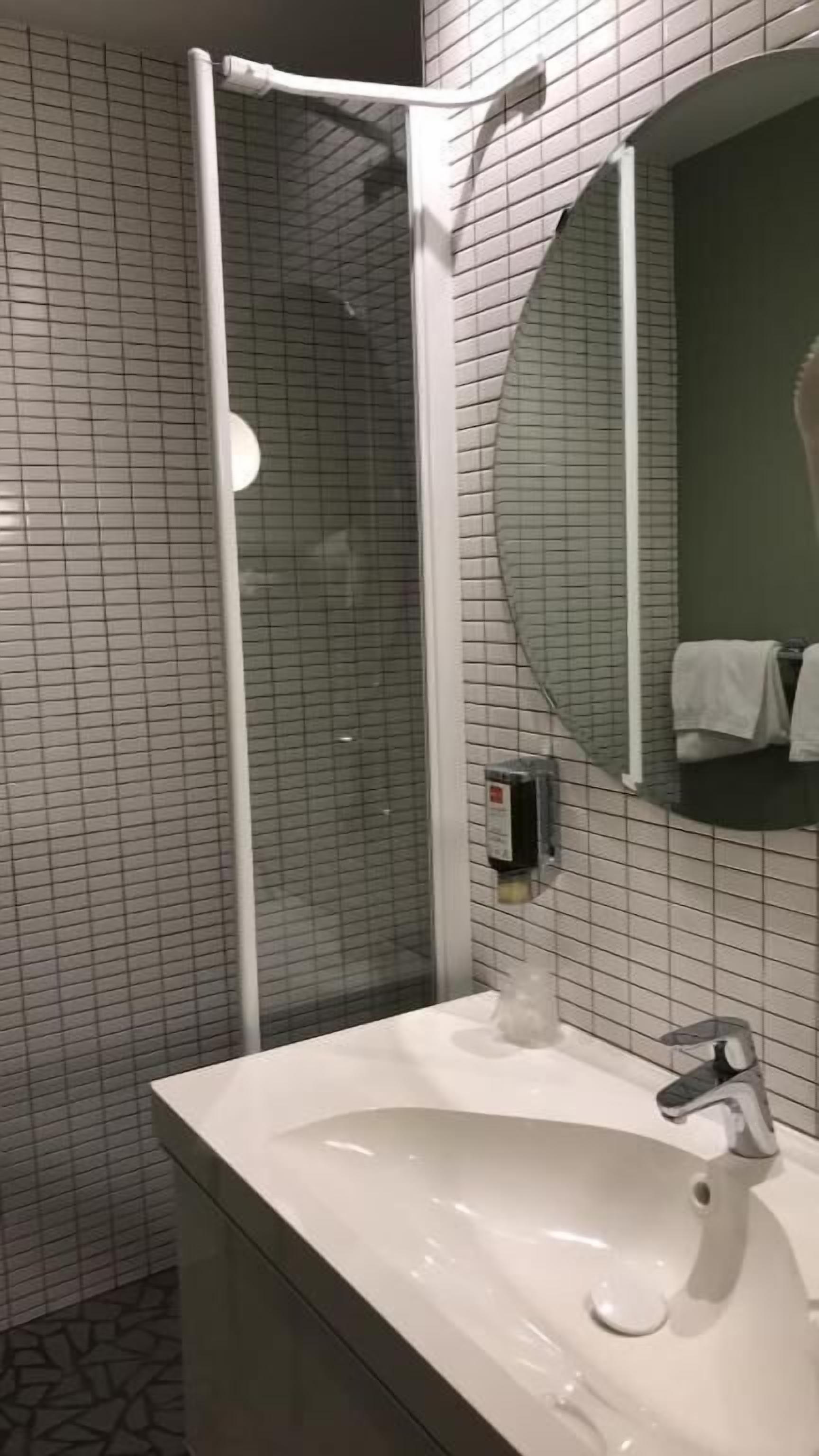 A modern bathroom with a glass shower enclosure, a white sink, and a round mirror.