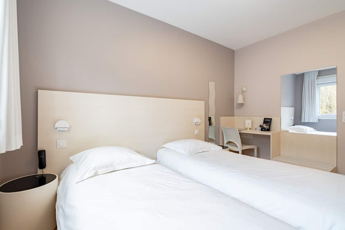 A modern hotel room with a large bed, a desk, and a window with curtains.