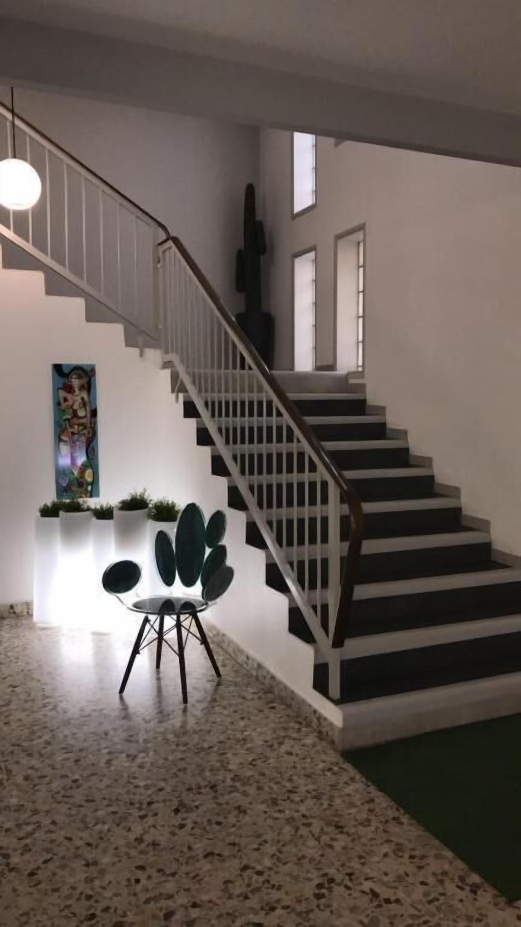 A staircase with a white railing, a wall-mounted sculpture, and a seating area with a chair and plants.