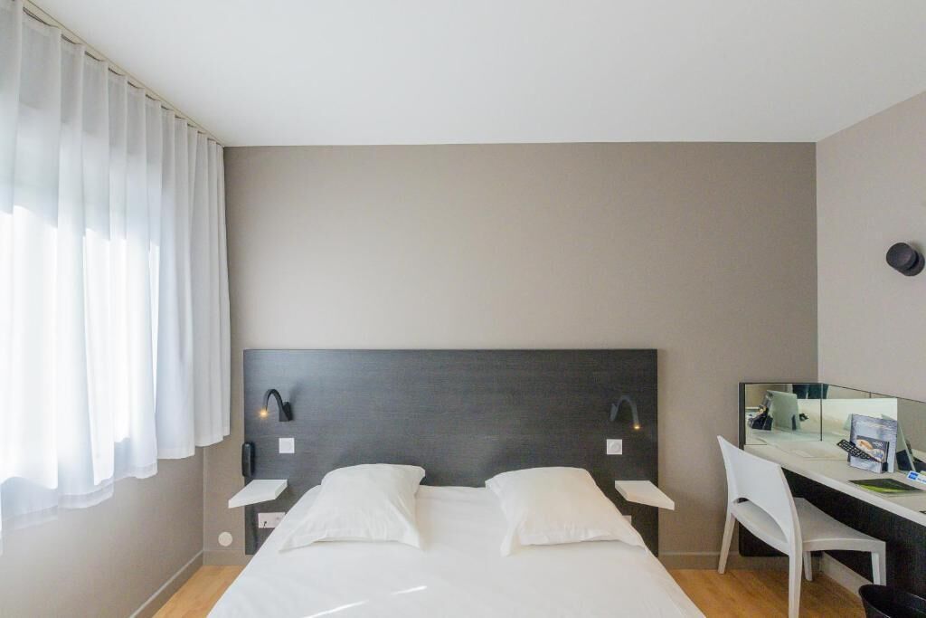 A modern hotel room with a large bed, a desk, and a chair.