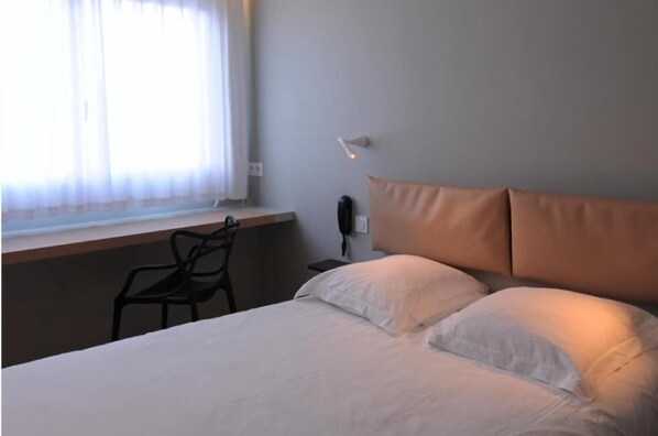 Une chambre d’hôtel avec un lit, une chaise, une table de chevet et une lampe.