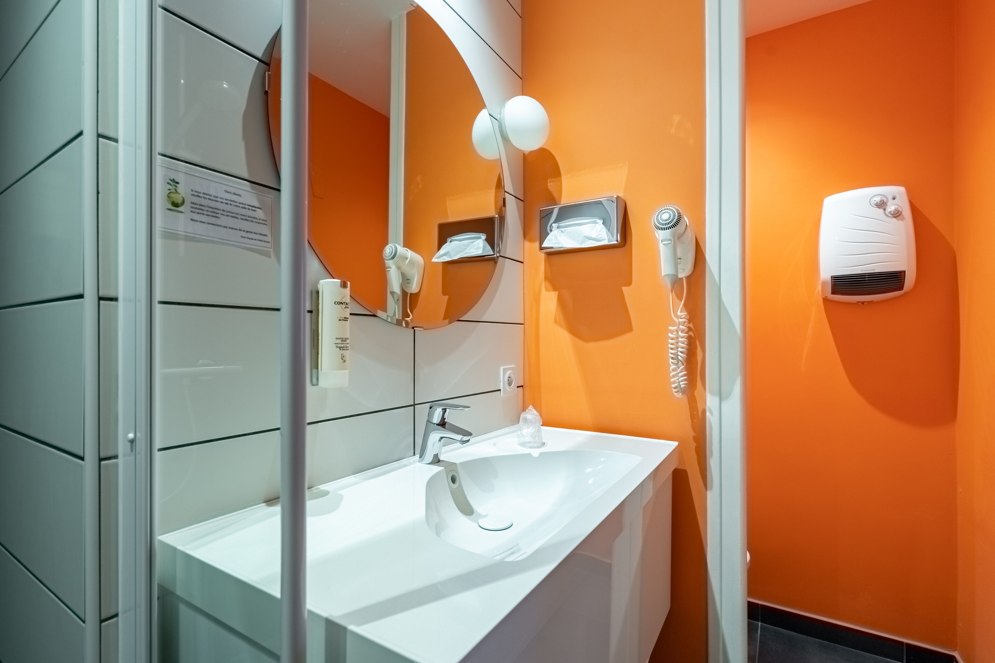 Un baño con lavamanos blanco, un espejo y un secador de pelo montado en la pared.