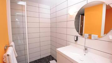 A bathroom with white tiled walls, a black and white patterned floor, a white sink, and a round mirror with an orange towel hanging on it.