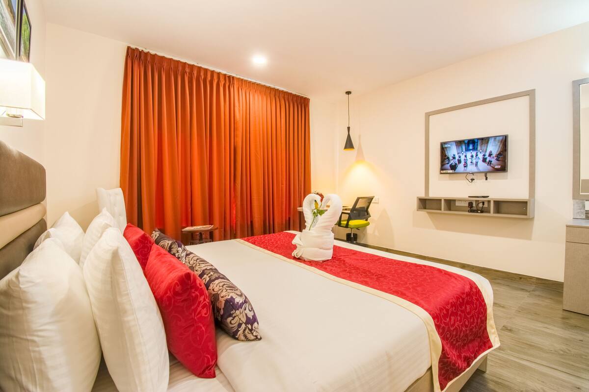 Ein Hotelzimmer mit einem großen Bett, einem an der Wand befestigten Fernseher und einem Schreibtisch mit Stuhl.