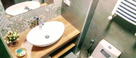 A bathroom with a wooden vanity, a white sink, a mirror, a toilet, and a shower area.