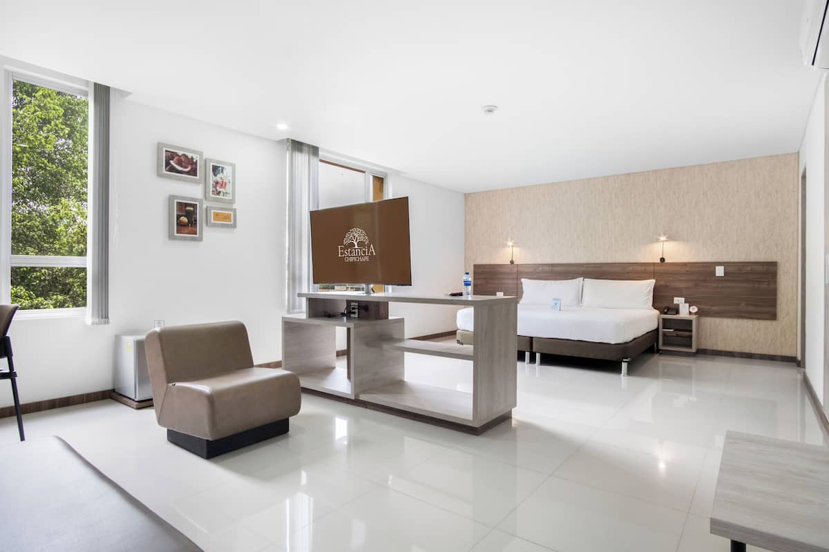 A modern hotel room with a bed, a desk, a chair, and a view of trees through the window.