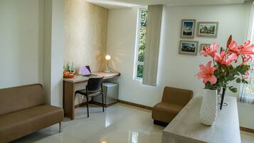 A modern living room with a sofa, a desk with a computer, a small refrigerator, and a vase with flowers.