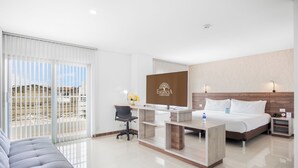 A hotel room with a bed, a desk, a chair, a nightstand, and a view of the outside. - Hotel Estancia Chipichape Cali (Cali)