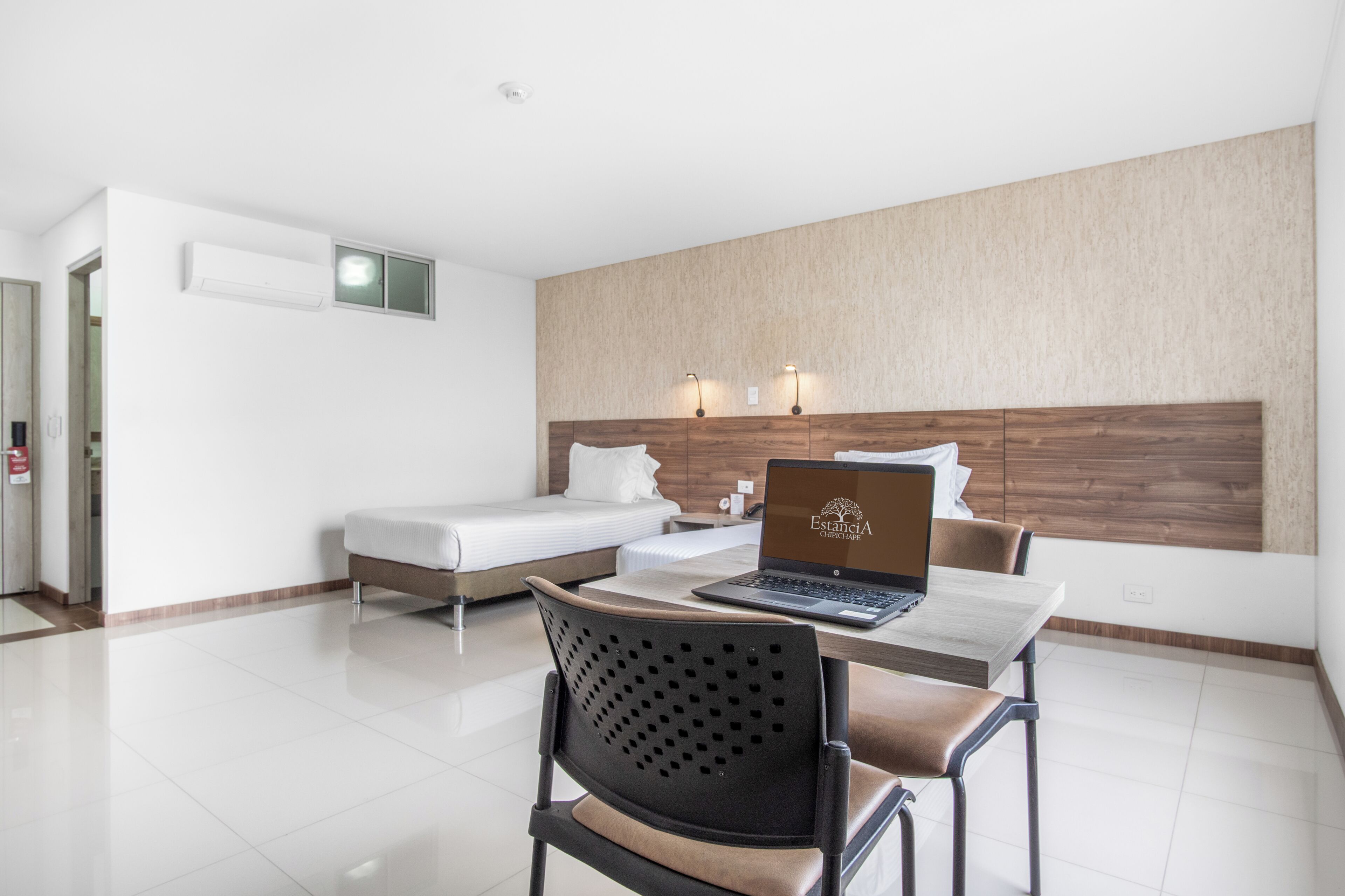 Een moderne hotelkamer met een bed, een bureau met een laptop, een stoel en een nachtkastje.