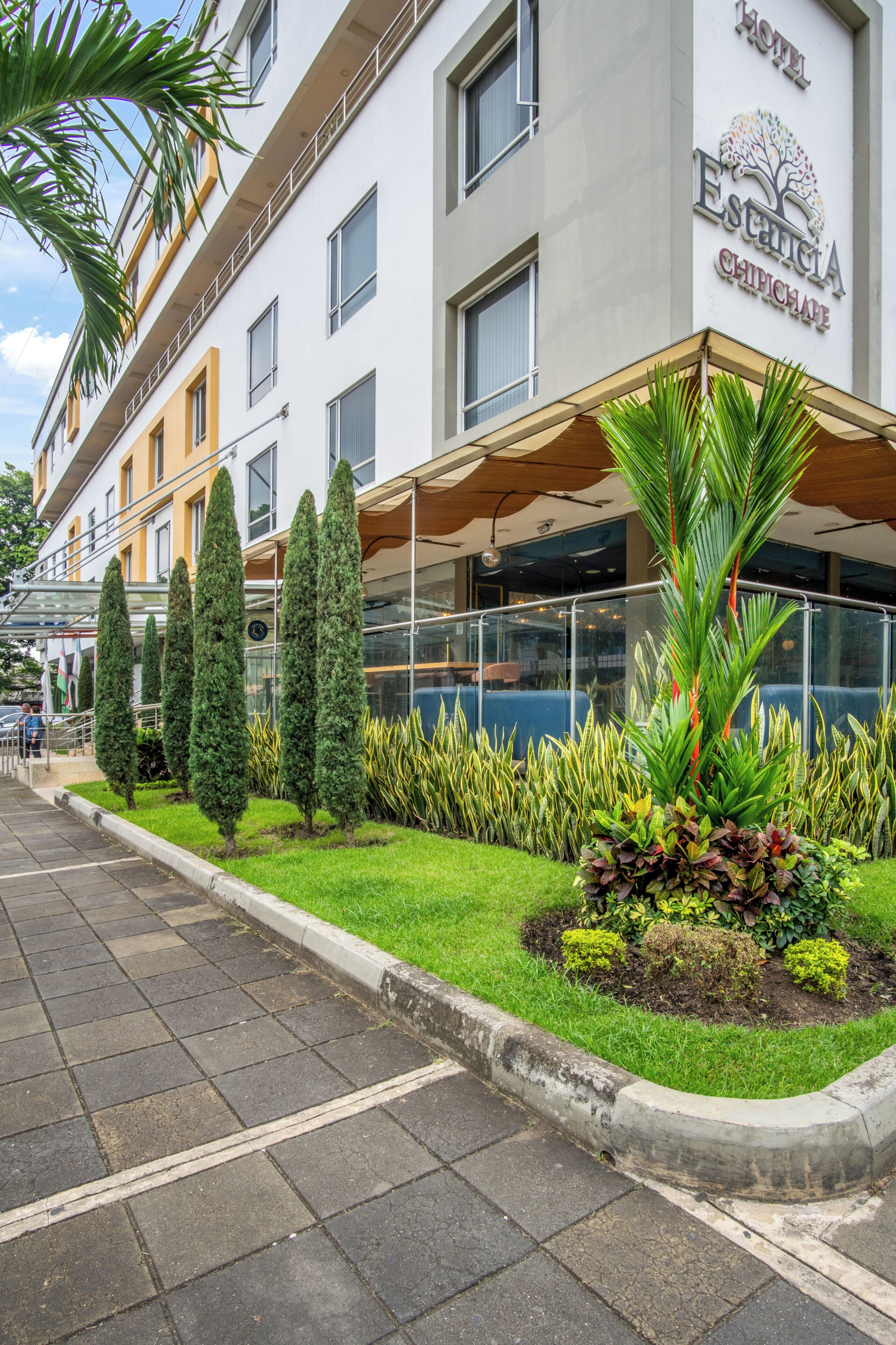A hotel with a modern facade, a well-maintained garden, and a clear sky.
