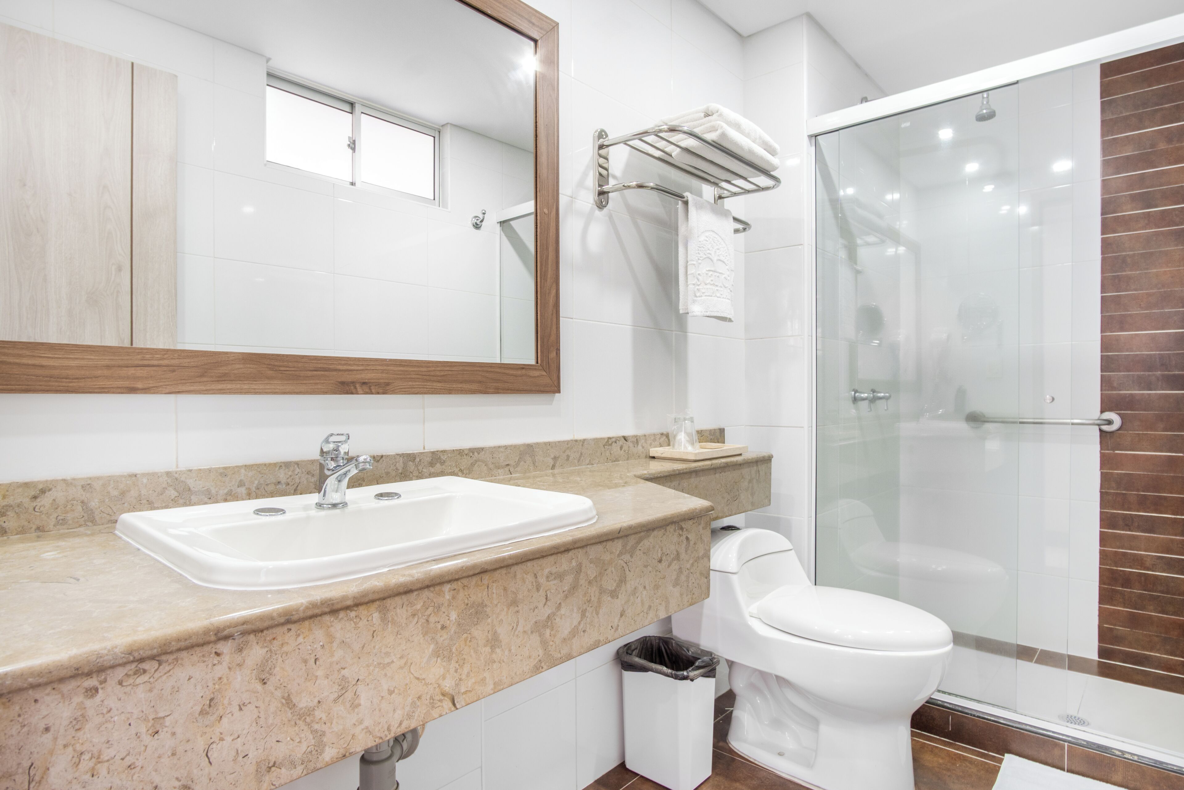 A bathroom with a sink, mirror, towel rack, toilet, and glass-enclosed shower.