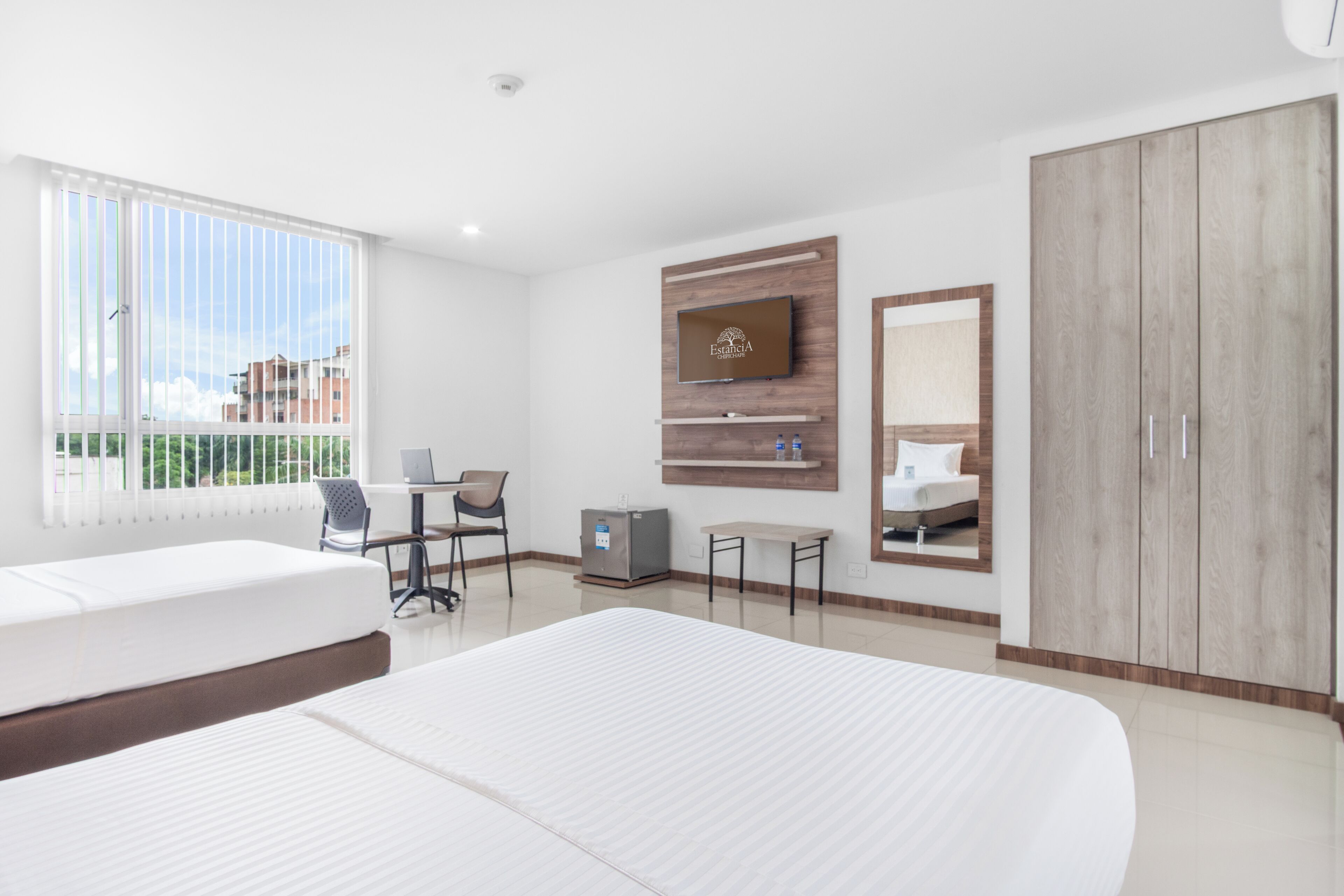 Habitación de hotel con dos camas, un escritorio, un televisor, un espejo y un armario.