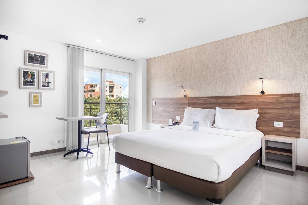 A modern hotel room with a large bed, a desk, and a view of the city.
