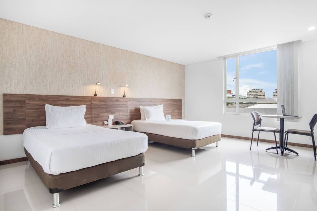 A hotel room with two beds, a desk, and a chair.