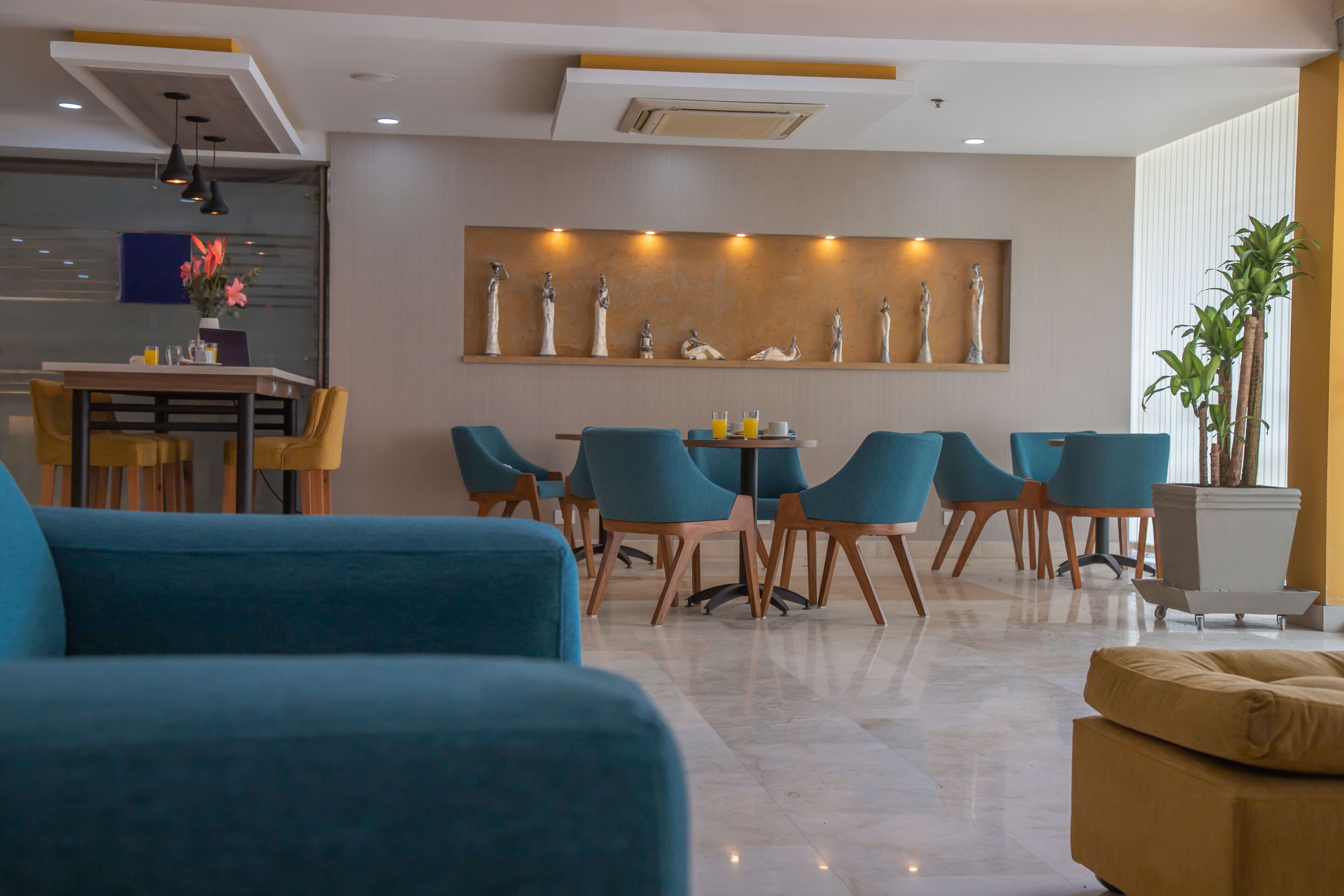 A modern living room with blue sofas, a dining area with teal chairs, and a decorative wall with statues.