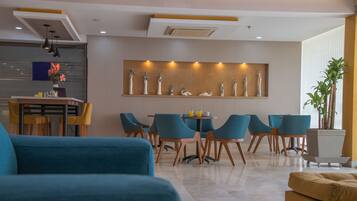 A modern living room with blue sofas, a dining area with teal chairs, and a decorative wall with statues.