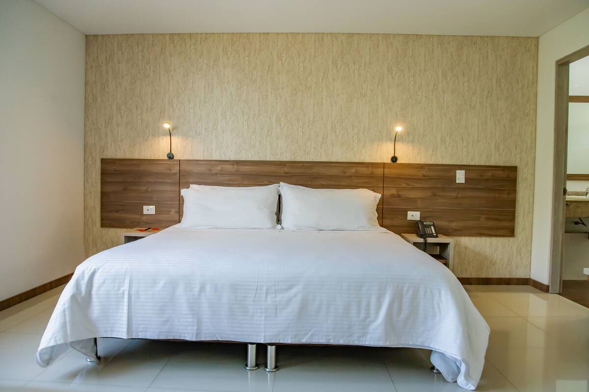 A large bed with a wooden headboard, two bedside lamps, and a nightstand with a telephone.