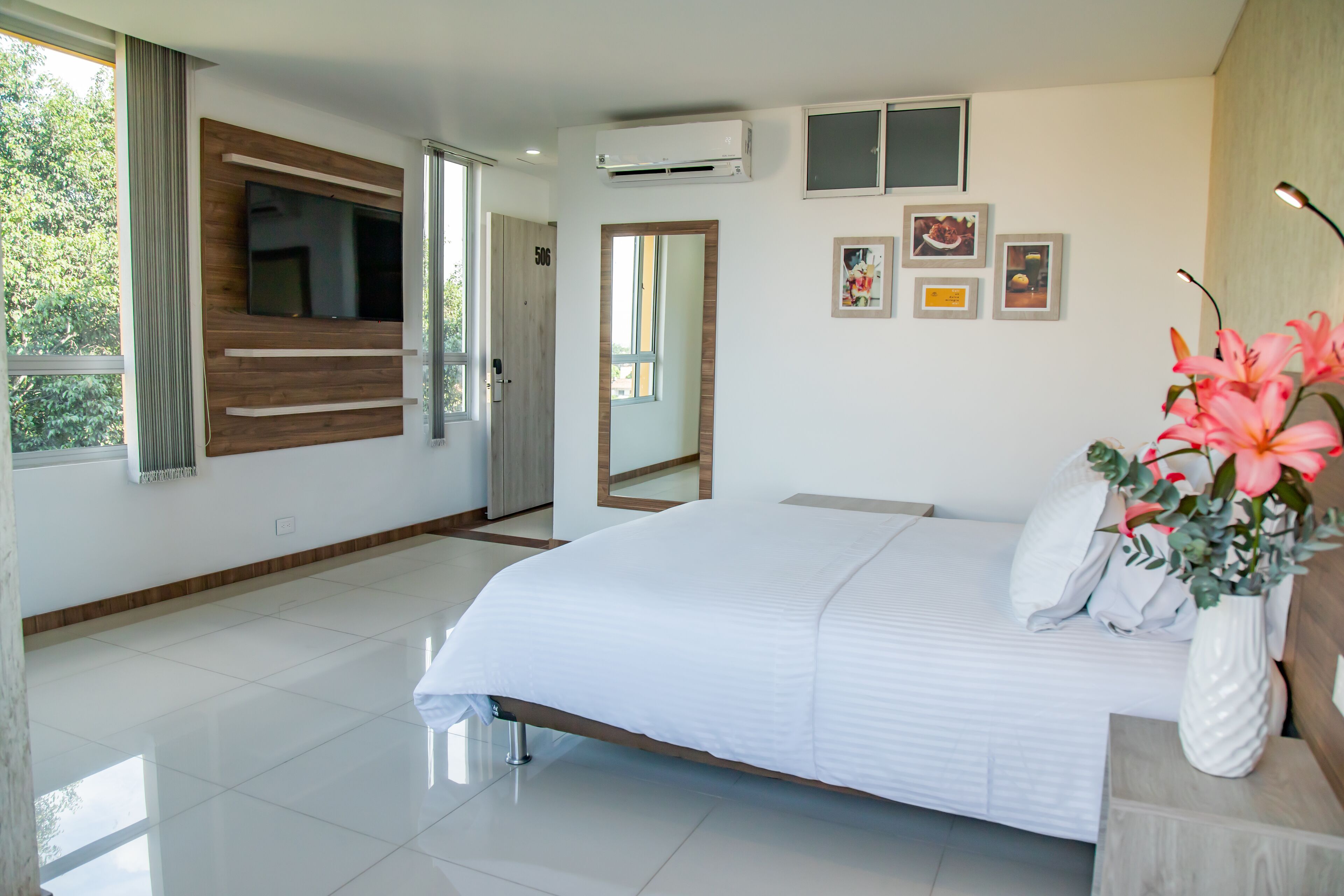 Habitación de hotel moderna con una cama grande, un televisor montado y vistas al exterior.