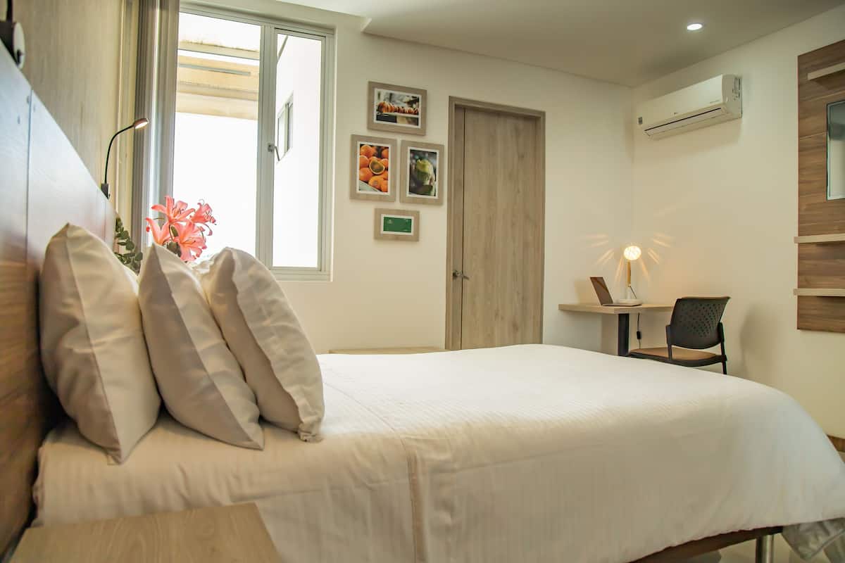 A bedroom with a bed, pillows, a desk, a chair, a window, and wall-mounted pictures.
