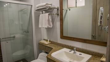 Un baño con cabina de ducha de vidrio, inodoro, lavabo con espejo y toallero con toallas dobladas.