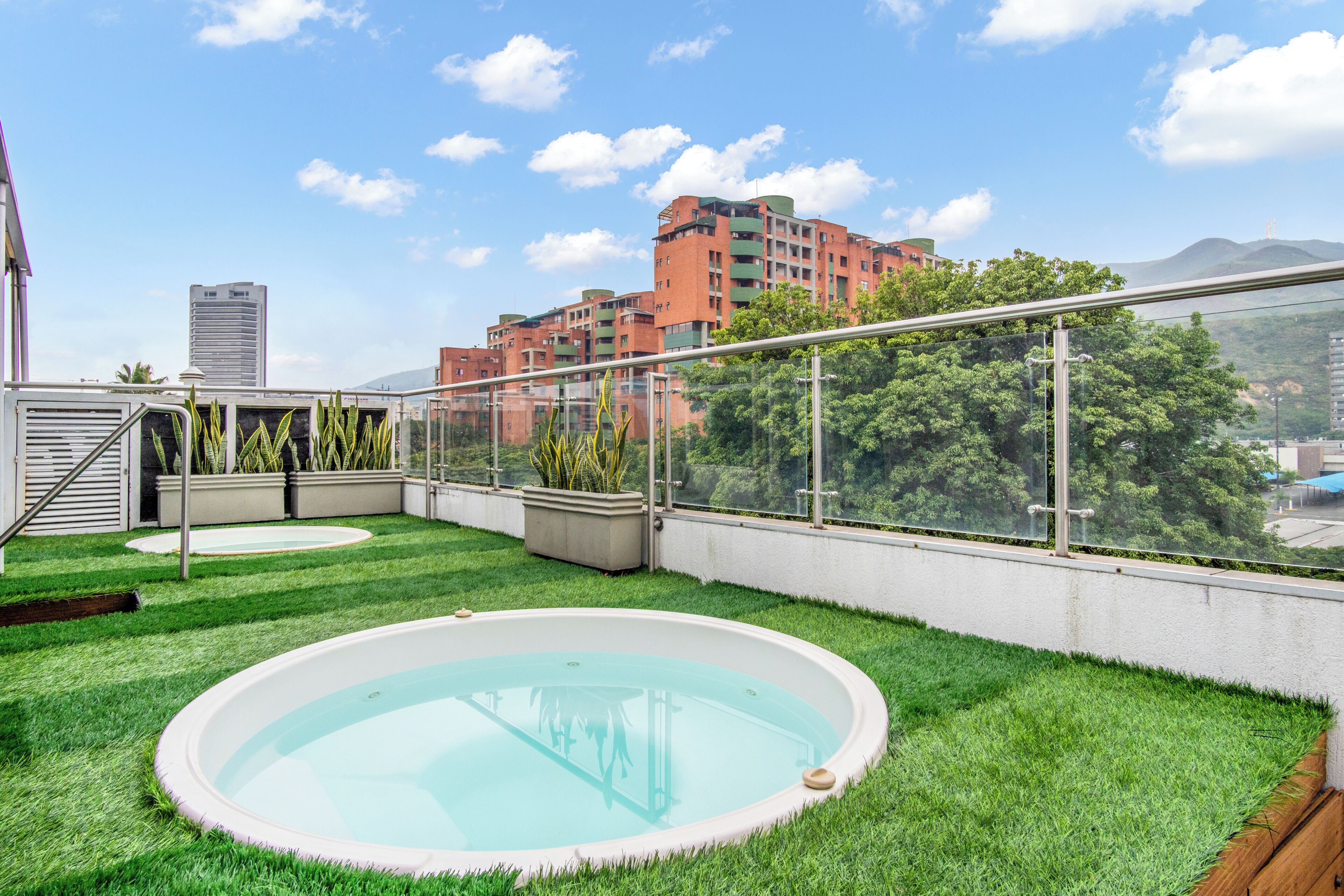 Ein Pool auf dem Dach mit Glasumrandung, umgeben von grünem Gras und Gebäuden im Hintergrund.