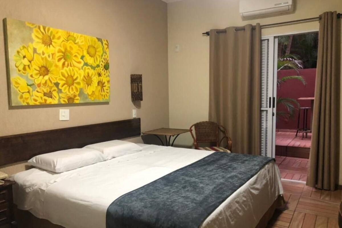 Ein Hotelzimmer mit einem Bett, einem Bild mit gelben Blumen, einem Tisch und einem Stuhl.