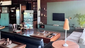 Amplia sala de estar con techo de madera, un conjunto de sofás, una mesa de centro y un televisor montado en una pared verde.
