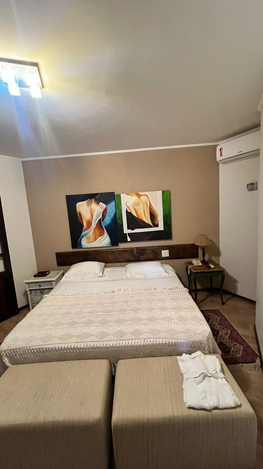 Habitación de hotel con una cama grande, dos mesitas de noche, una lámpara y dos cuadros en la pared.