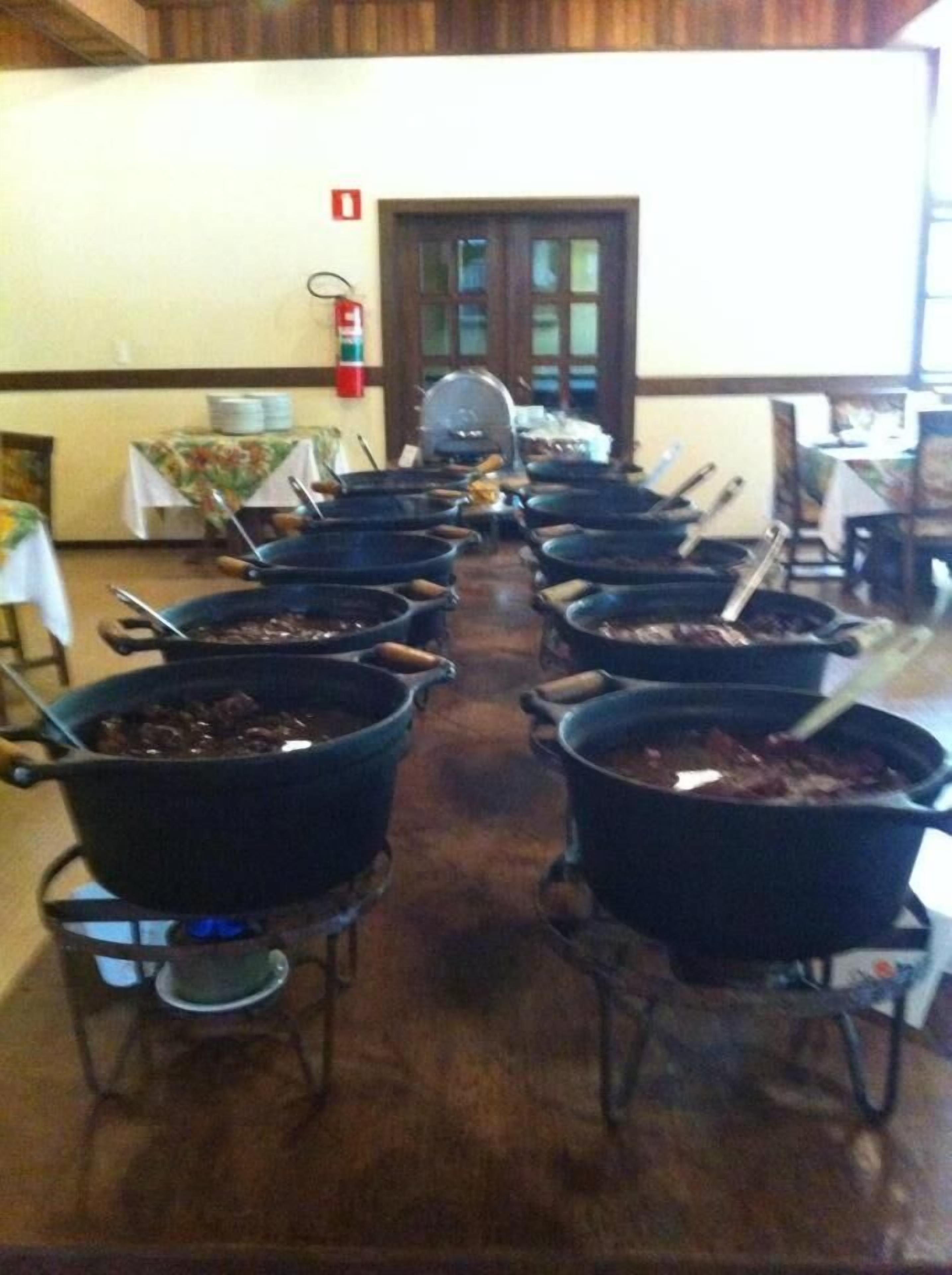 Una larga mesa con varias ollas grandes, probablemente para cocinar o servir comida, en una habitación con paredes de madera y una puerta al fondo.