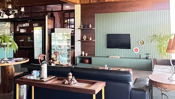 Una sala de estar moderna con techo de madera, un sofá negro, una mesa de centro de madera y un televisor montado en la pared.