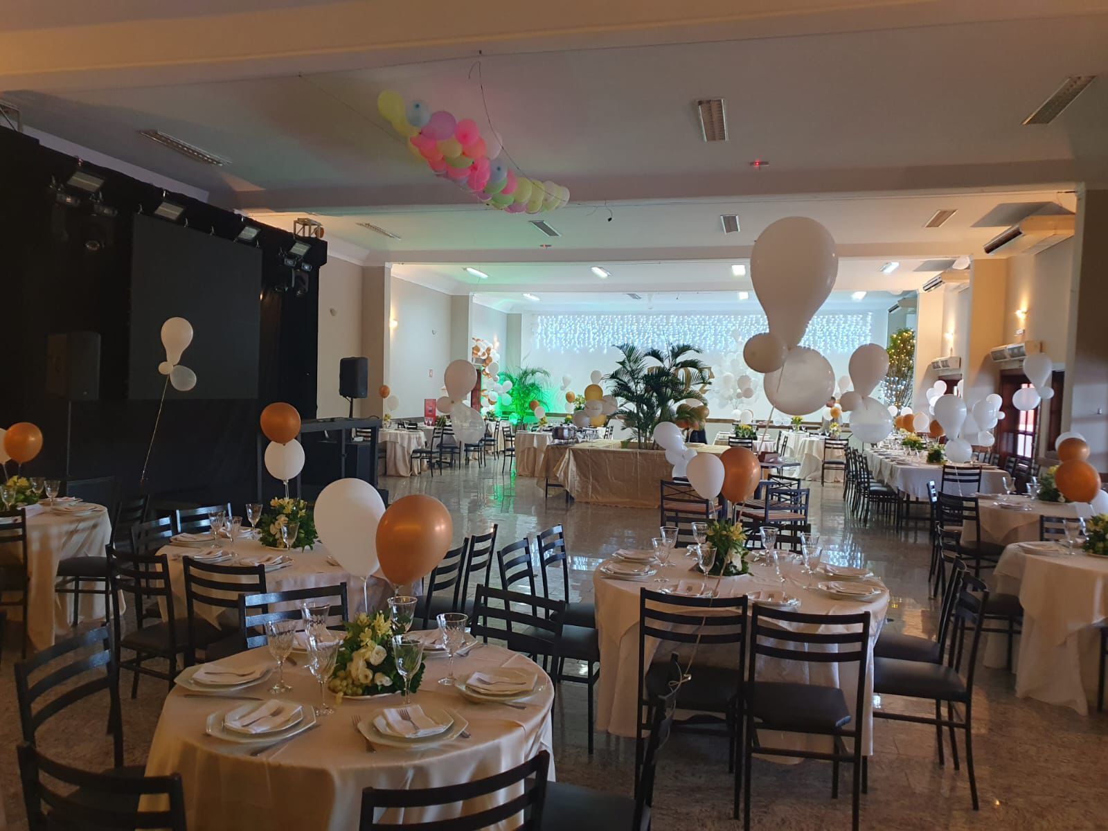 A banquet hall with round tables set for dining, decorated with balloons and floral centerpieces.