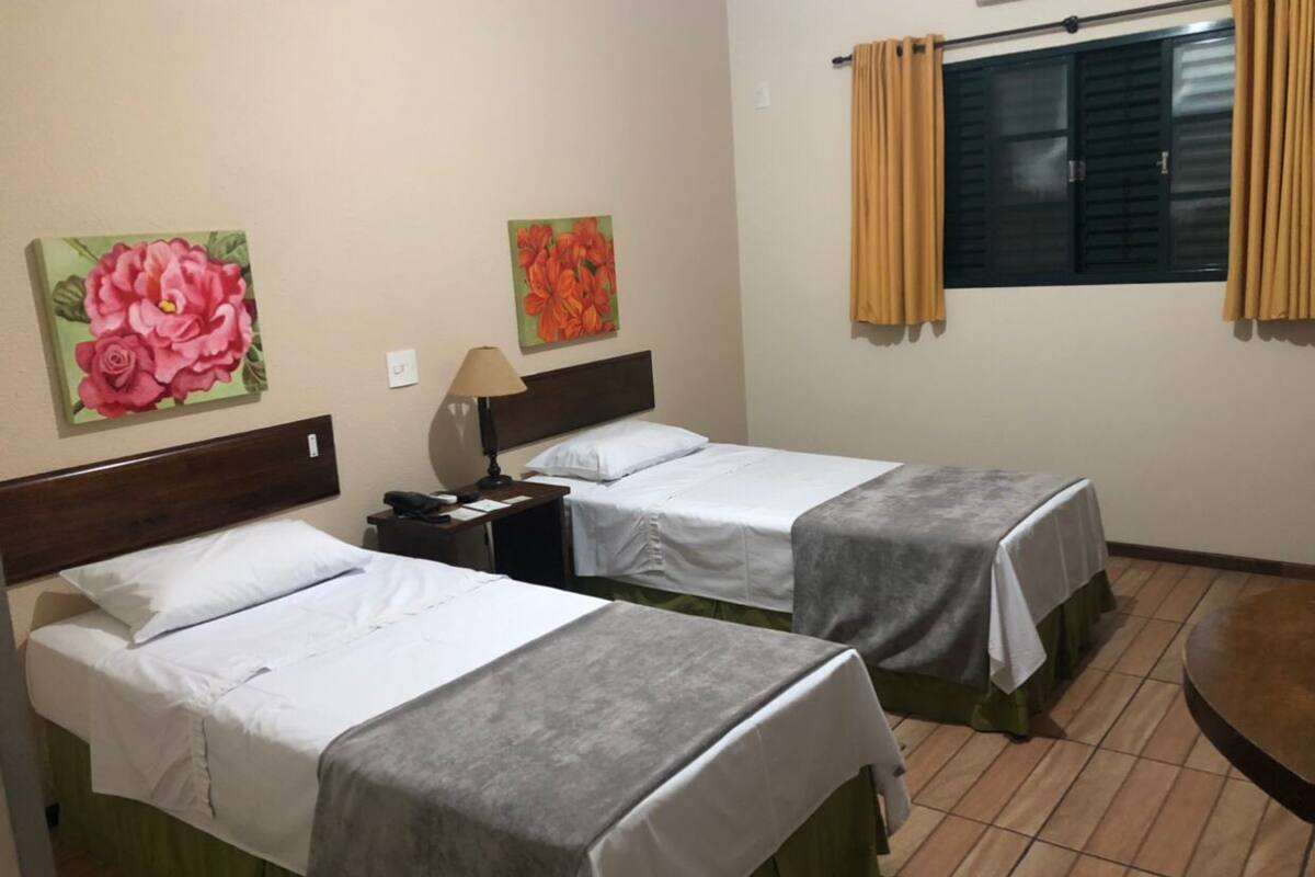 Ein Hotelzimmer mit zwei Betten, einem Nachttisch, einer Lampe und zwei floralen Bildern an der Wand.
