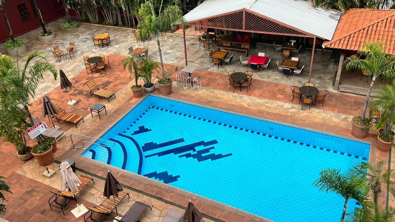 An outdoor swimming pool with lounge chairs and tables, surrounded by potted plants and a covered seating area.