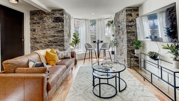 Ein modernes Wohnzimmer mit einer Wand aus Naturstein, einem Ledersofa, einem Glastisch und einem Essbereich mit Stühlen und einem Tisch.